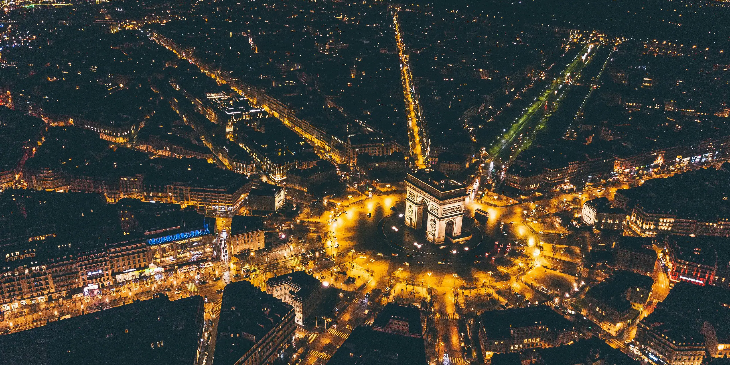 The Arc de Triomphe and the avenues of Paris from above, at night.