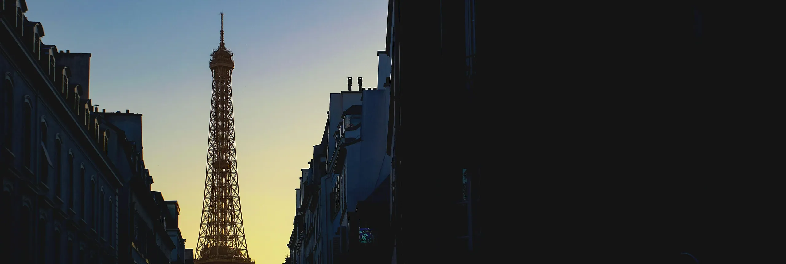The Eiffel Tower at the end of a Paris street at dusk.